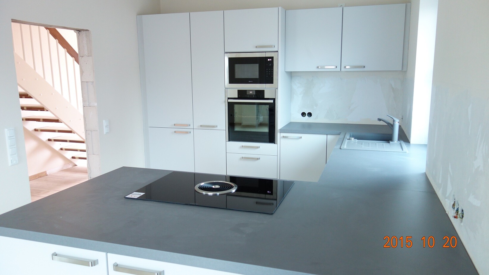 Modern kitchen with island, induction cooktop, oven, microwave and sink.