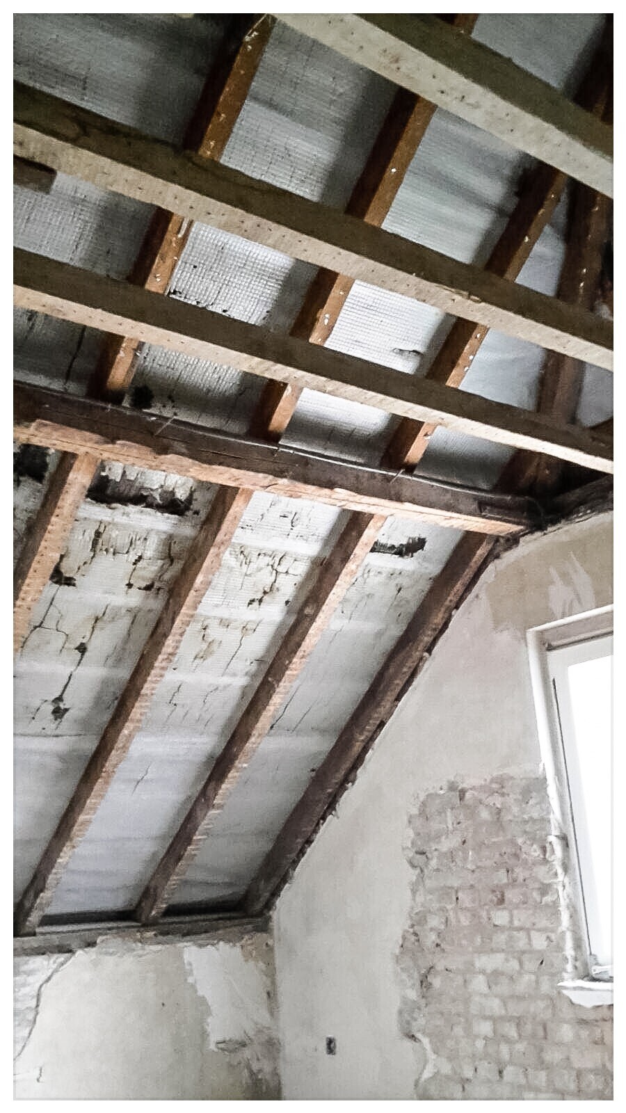 Sicht auf Dachstuhl mit Holzbalken, Dämmung zwischen Sparren und verputzten Wänden