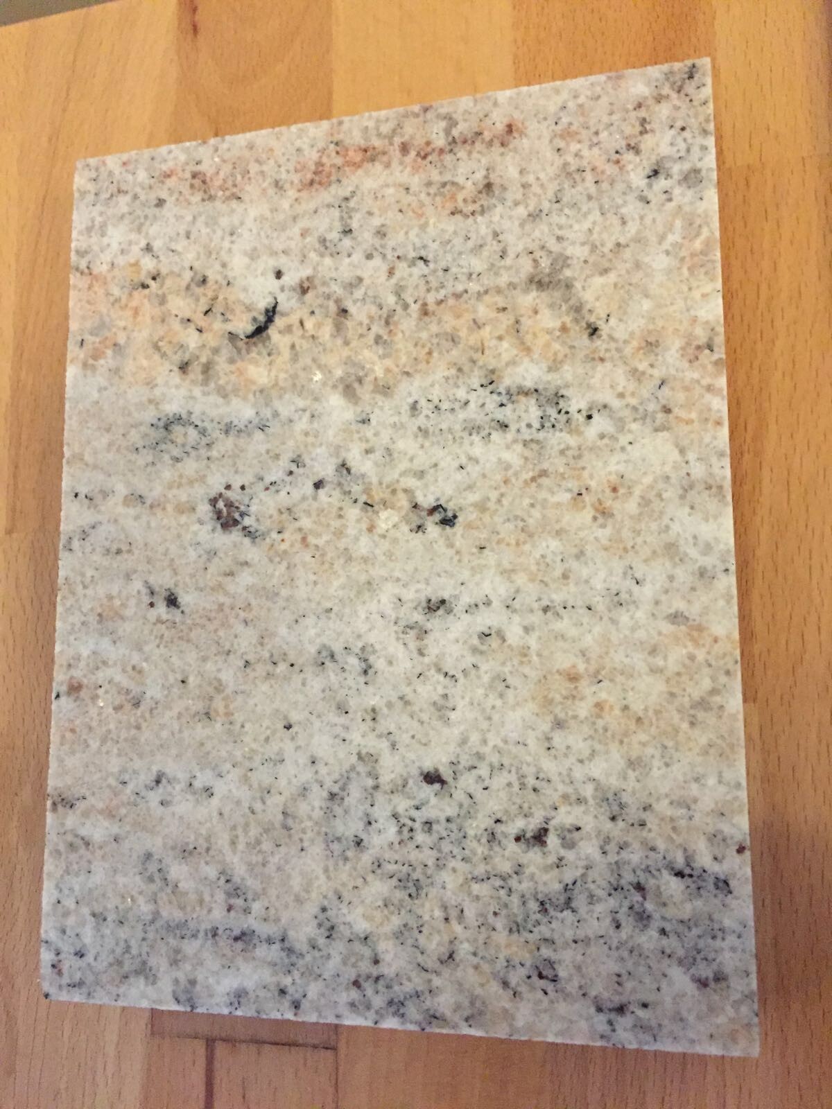 Granit-Probestück in grau-weiß gemustert auf Holzboden.