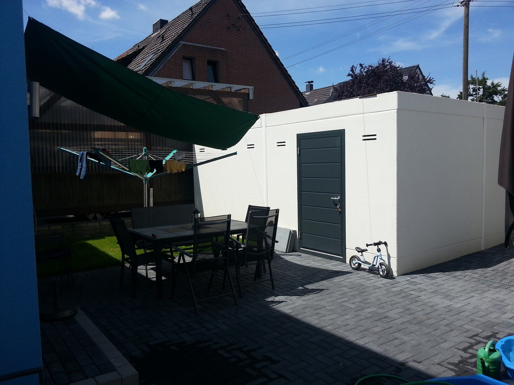 Courtyard with dining table and chairs, clothesline, green sunshade, white concrete wall, children's bicycle
