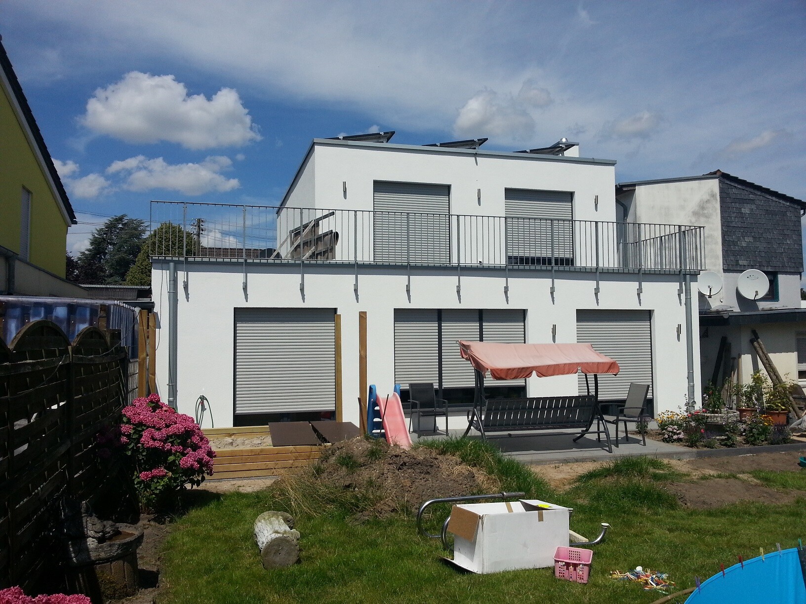 White modern house with rooftop terrace, garden furniture under awning, and toys in the garden