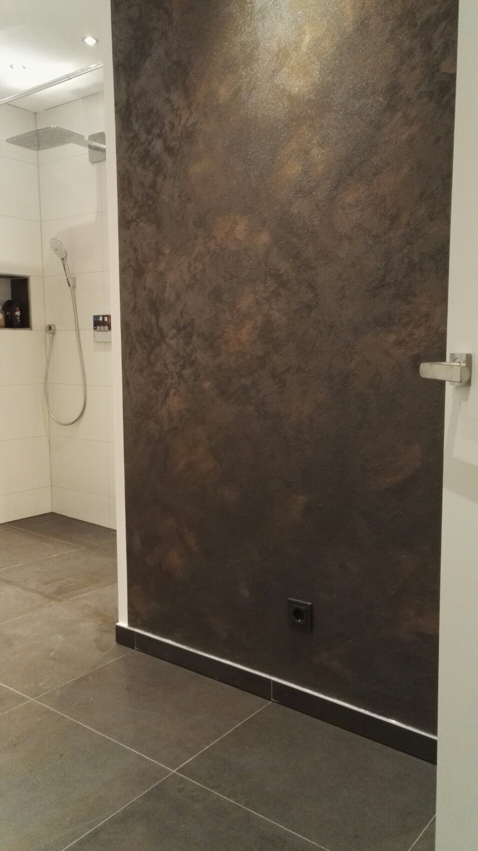 Dark textured bathroom wall next to a walk-in shower with white tiles.