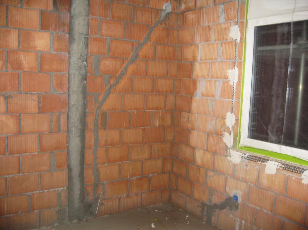 Unplastered interior with raw brickwork, concrete column, and window frame