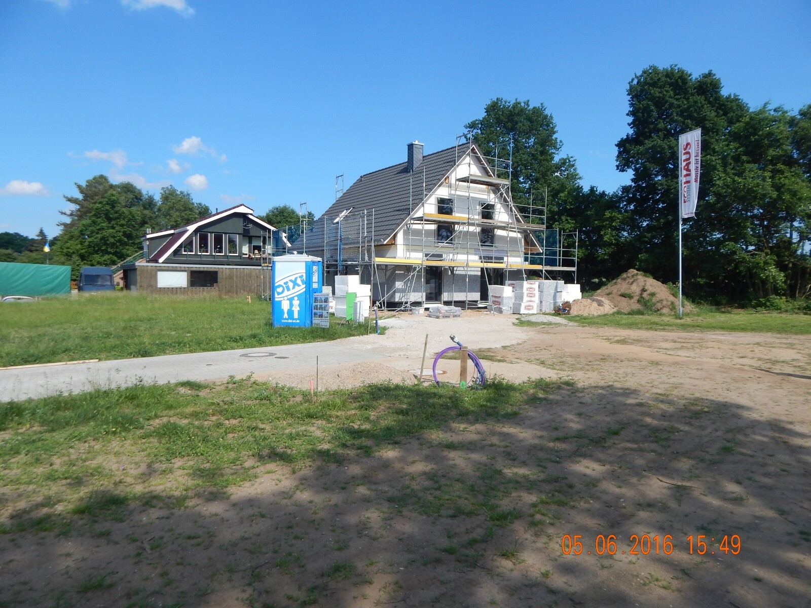 House under shell construction with scaffolding, building materials and site storage on a construction site under blue sky