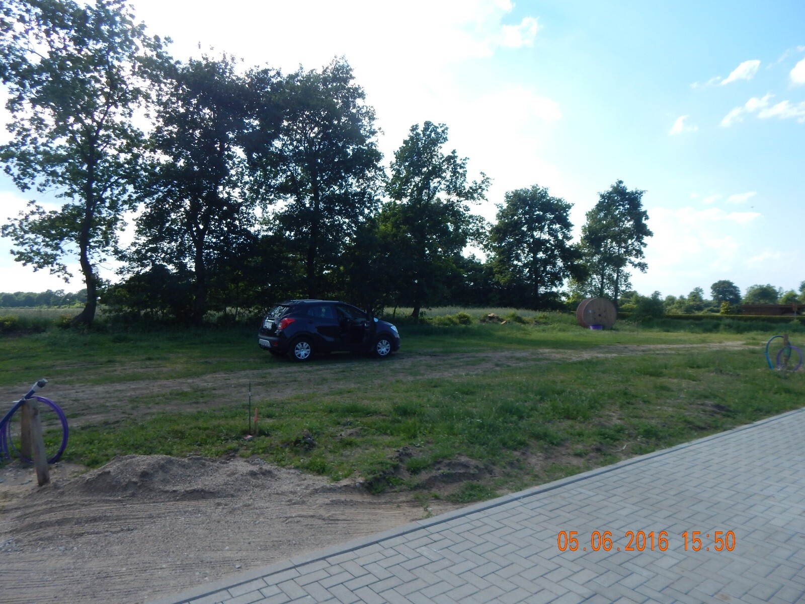 Unbuilt building plot with parked car, row of trees in the background and construction materials