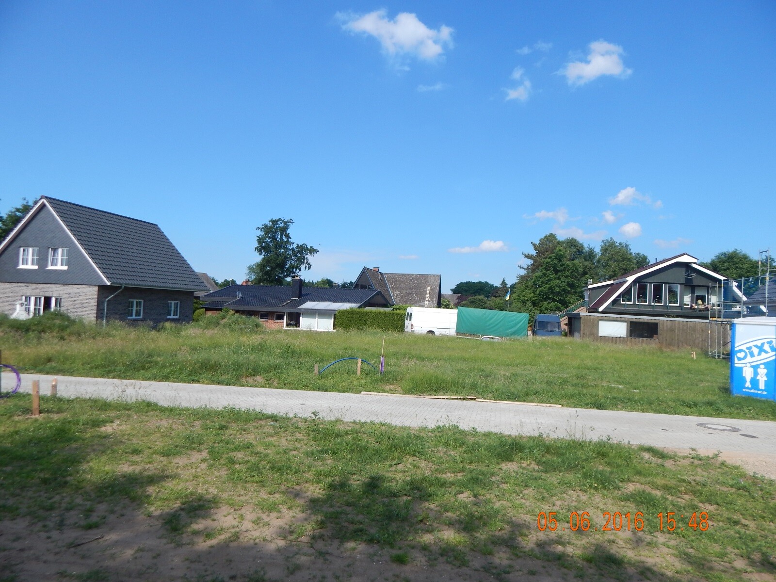 Construction site with shell and finished houses, green landscape and blue sky.