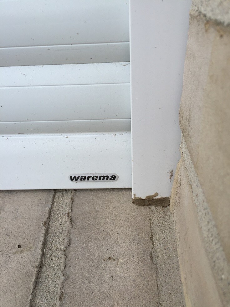 Weisser Rolladenrahmen vor Betonwand mit Warema-Logo am unteren Rand.